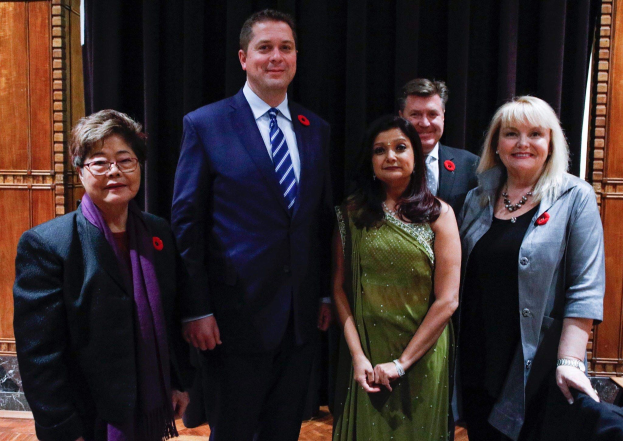 Gruppe von Menschen vor einem schwarzen Vorhang mit einem hölzernen Hintergrund, die scheinbar Mitglieder der Liberalen Partei bei einer Versammlung sind.