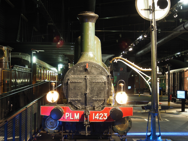 Eine Dampflokomotive in einem Museum ausgestellt, umgeben von einem Metallzaun mit Besuchern in der Nähe.
