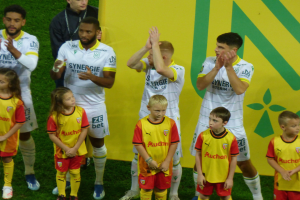 Gruppe von Fußballspielern in Uniformen, die auf einem Feld klatschen, mit einem "Ligue 1"-Schild im Hintergrund, das einen Sieg feiert.
