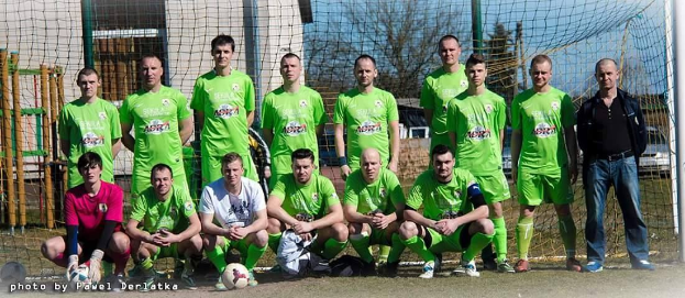 Gruppe von Männern in grünen T-Shirts auf einem Fuballfeld in der Nähe eines Torpfostens, einige hocken, mit einem Ball vor ihnen.