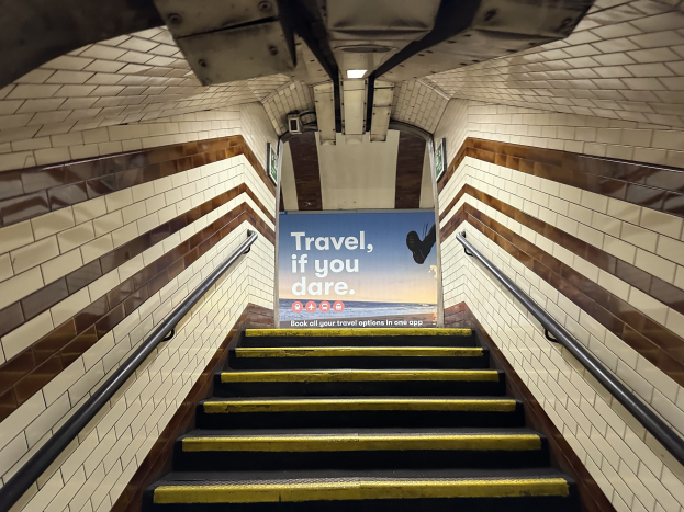 Eine Treppe in einer U-Bahn-Station mit einem Schild "Reise, wenn du wagst" oben, flankiert von Geländern und sichtbaren Stationwänden.