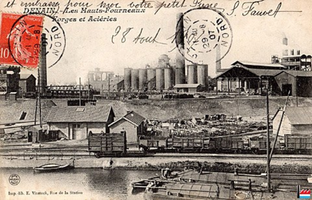 Alte Postkarte zeigt eine Fabrik mit Häusern, Strommasten, Schiffen und Wasser im Hintergrund sowie Stempel und handgeschriebene Texte.