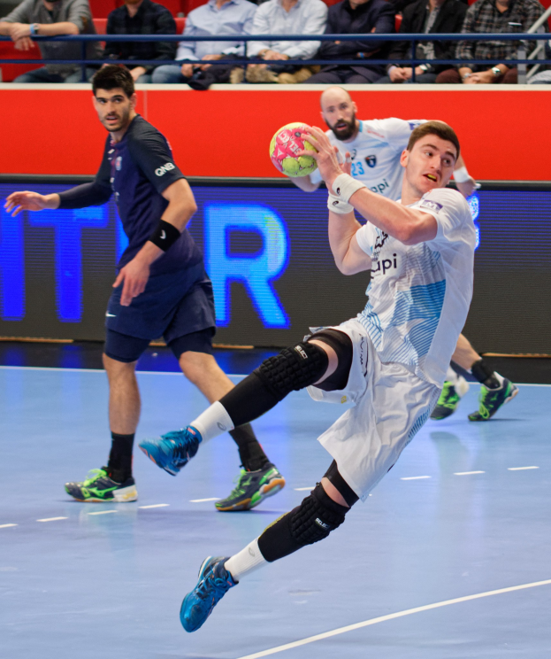 Eine Gruppe von Männern spielt Handball auf einem Feld während der Futsal-Weltmeisterschaft 2019, mit Zuschauern im Hintergrund und einer Anzeigetafel mit Spielplan.