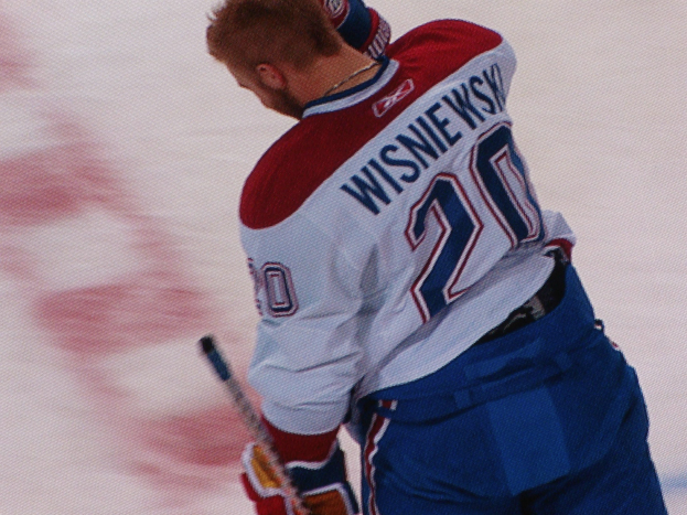 Professioneller Eishockeyspieler in einem "Wisniewski"-Trikot, der mit konzentrierter Miene auf dem Eis einen Hockey-Schläger hält.