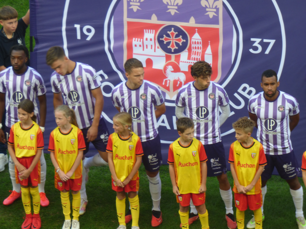 Eine Gruppe junger Menschen, die auf einem Fußballfeld zusammenstehen, mit einem Banner dahinter, auf dem 'Preston Primary School Football Team' steht.