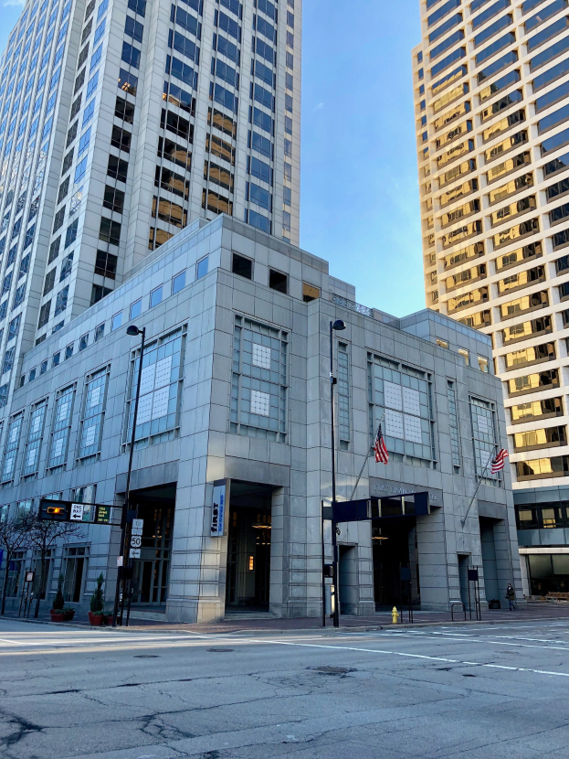 Großes Backsteingebäude mit vielen Fenstern, als Hauptsitz der Chicago Public Library bezeichnet, auf einer Stadtstraße mit Straßenmöbeln, Bäumen und einem bewölkten Himmel.