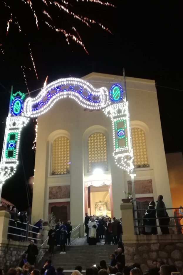 Menschen vor einem Gebäude mit beleuchtetem Bogen, Treppe und Topfpflanzen, die Feuerwerk an Silvester beobachten.