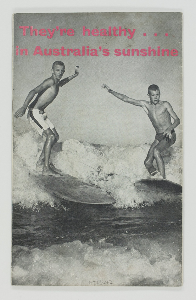Zwei Jungs stehen auf Surfbrettern im Wasser mit einem Plakat im Hintergrund, das 'sie sind gesund in Australien's Sonne'