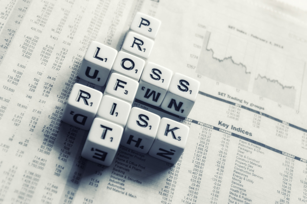 Kreuzworträtsel mit den Wörtern "Verlust, Risiko und Risiko" über einer mit Text und Zahlen gefüllten Zeitung, das Finanzplanung und Risikomanagement suggeriert.