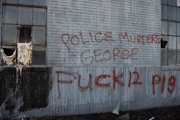 Graffiti auf einer Gebäudewand lautet "Polizei ermordet George Fuck 12 P19" mit Fenstern und verstreuten Gegenständen davor.