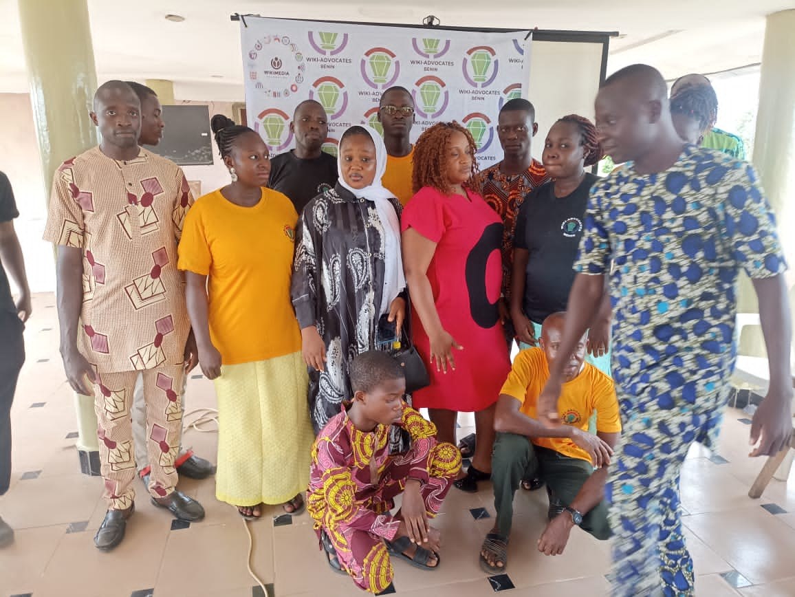 Gruppe von Menschen vor einem Banner mit der Aufschrift "Advocates in Ghana: Ein Schritt-für-Schritt-Führer" mit Stühlen, Säulen, einem Fernseher und einer Decke mit Deckenleuchten im Hintergrund.