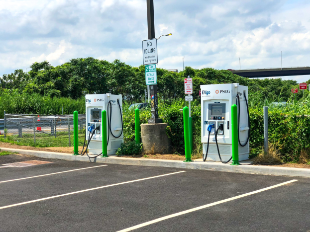 Ladestation für Elektrofahrzeug auf einem Parkplatz mit umgebenen Infrastruktur und einer Brücke im Hintergrund.