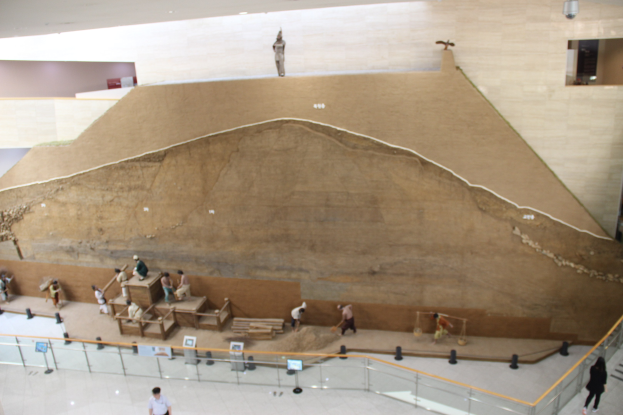 Großer Felsformation-Grabhügel in einem Museum mit Informationsschildern, einer Treppe und Deckenbeleuchtung ausgestellt.