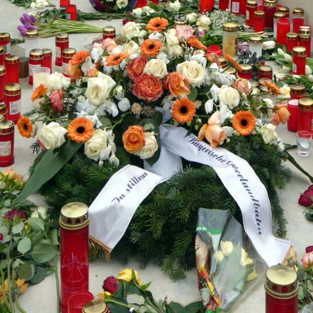 Mahnmal in Berlin mit Blumen und Kerzen vor einer Wand aufgestellt.