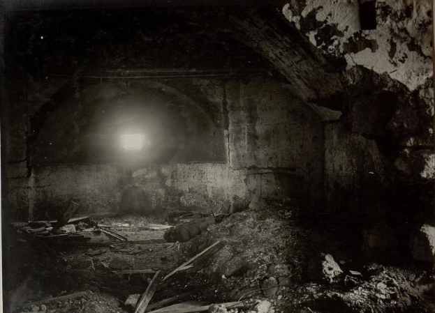 Ein Schwarz-Weiß-Foto eines zerfallenden Tunnels in den Berliner Mauerruinen mit Schutt auf dem Boden und einem Licht am Ende.