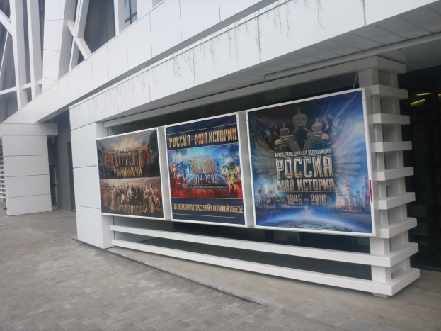 Großes Werbeplakat an der Seite eines Gebäudes für die Eröffnungsfeier der Olympischen Spiele in Moskau, mit beleuchtetem Gebäude auf der rechten Seite und sichtbarem Boden.