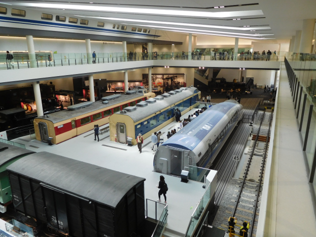 Eine große Museumsausstellung zeigt verschiedene Züge in verschiedenen Größen und Farben, die von Besuchern auf mehreren Ebenen und vom Boden aus betrachtet werden.