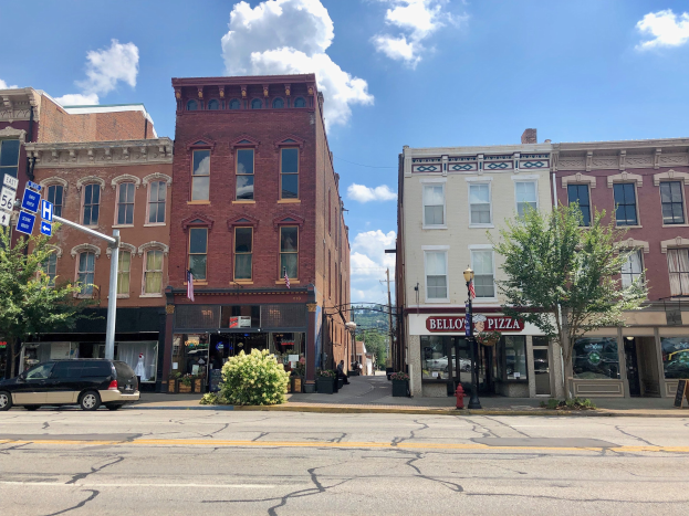 Eine Straße mit parkenden Autos, Gebäuden, Bäumen, Laternen, Schildern und einem Feuerhydranten unter einem bewölktem Himmel, die ein kommerzielles Grundstück repräsentiert.