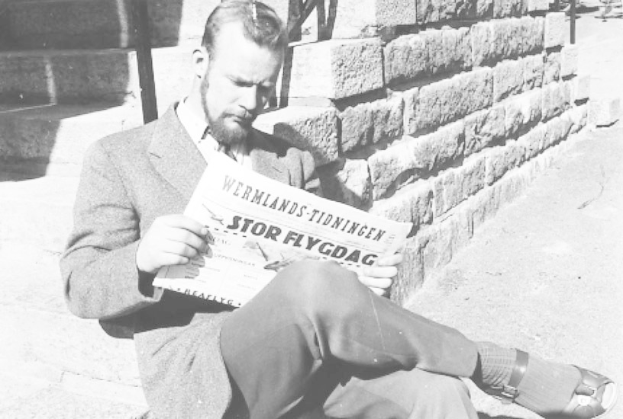 Mann in Anzug sitzt auf Treppe und liest Zeitung mit ernstem Gesichtsausdruck in Schwarz-Weiß-Fotografie.