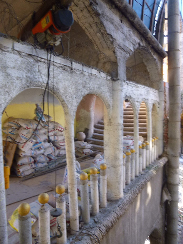 Altes Gebäude mit Rundbogenfenstern, Säulen, Treppen, Geländern, verstreuten Werkzeugen, Materialien und einer Maschine mit Drähten oben.