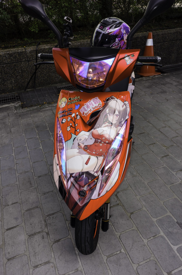 Orangeroller auf einer Straße mit Helm darauf, einer Verkehrskegel, einer Wand und Bäumen im Hintergrund.