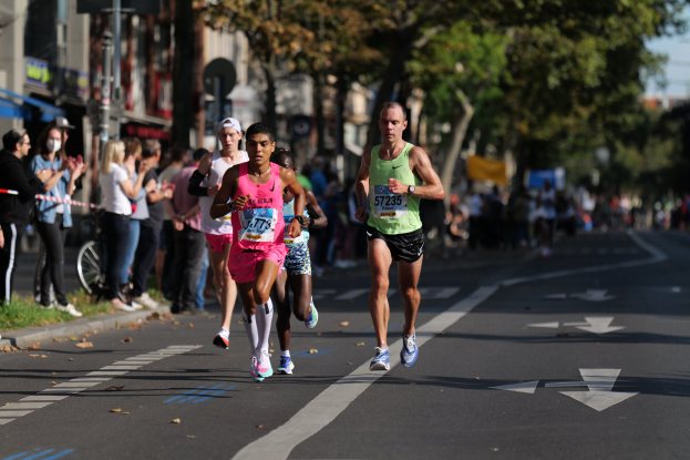 Eine Gruppe von Menschen, die bei einem Marathon durch die Stadt laufen, mit Zuschauern und unscharfen urbanen Hintergrundelementen.