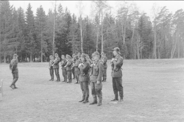 Schwarzes und weißes Bild einer Gruppe von Männern in Mützen mit Gewehren, die in einem Feld mit Bäumen und einem klaren Himmel im Hintergrund stehen.