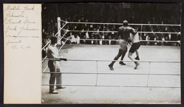 Schwarzes und weißes Foto von zwei Boxern in einem Ring mit einem Schiedsrichter auf der linken Seite und Zuschauern im Hintergrund, betitelt "Jack Johnson vs Frank Morgan" in der oberen linken Ecke.