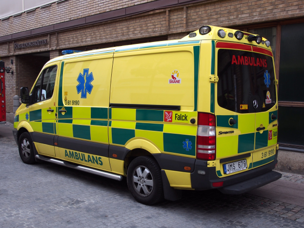 Ambulanz auf der Straße vor einem Backsteingebäude mit Text, mit einem sichtbaren Feuerlöscher auf der linken Seite.