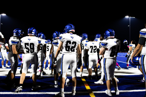 Gruppe von Fussballspielern in Helmen und Stiefeln auf einem Feld unter Flutlicht, bereit für ein Spiel.