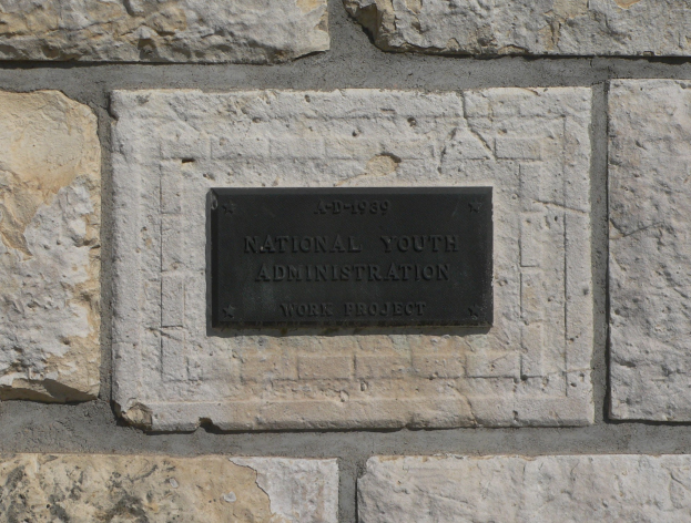 Steinwand mit einem rechteckigen Schild, auf dem in fetten weißen Buchstaben 'National Youth Administration' steht.