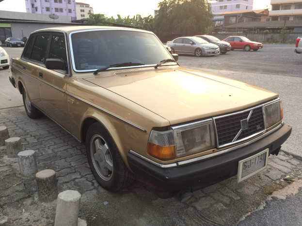 Ein goldfarbener Wagen, der auf der Seite einer Straße mit Gebäuden, Bäumen und einem klaren blauen Himmel im Hintergrund geparkt ist.