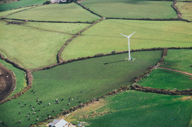 Luftaufnahme einer Windturbine in einer grünen Wiese mit Tieren, Häusern und einer lückigen Graslandschaft in Irland.