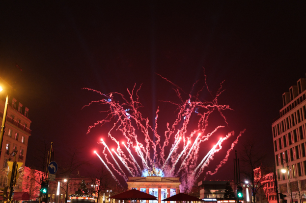 Eine belebte Straßen Szenerie in Berlin an Silvester, gefüllt mit Menschen, Fahrzeugen und Gebäuden, beleuchtet von Lichtern und Feuerwerk am Himmel.