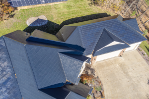 Luftaufnahme eines Hauses mit in das Dach integrierten Solarpanelen, umgeben von Bäumen, Gras und einem Zaun.