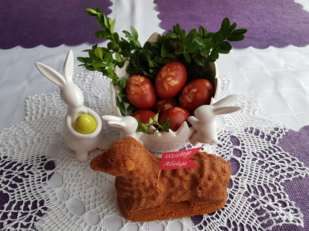 Ein mit einer Decke bedeckter Tisch trägt eine Schüssel voller bunter Ostereier mit Osterhasen-Figuren darauf.