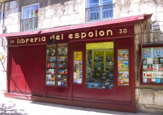 Ein zweistöckiges Gebäude mit einer Schaufensterfront, die ein rotes Vordach trägt, auf dem 'Libreria del Espolon' steht und ordentlich arrangierte Bücher im Inneren zeigt.