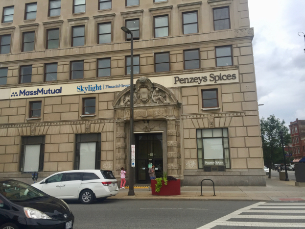 Hauptsitz der Massachusetts Mutual Financial Group mit parkenden Autos davor, umgeben von Straßenlaternen, Autos, Fußgängern, Grünpflanzen, Bäumen und einem bewölkten Himmel.