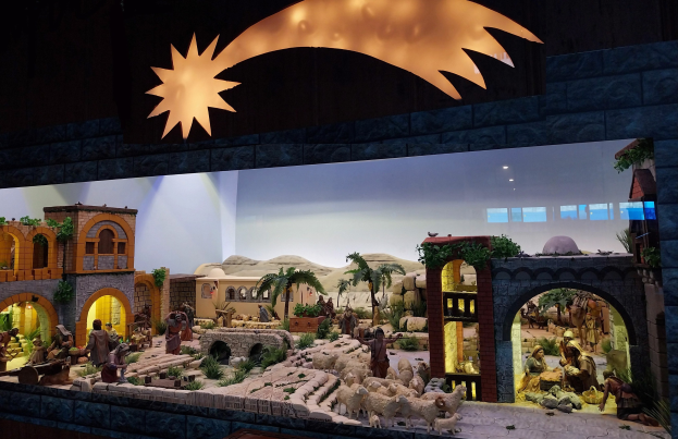 Eine Krippe-Ausstellung im Museum mit Menschen, Tieren, Häusern, Bäumen und anderen Gegenständen, beleuchtet von einer Deckenbeleuchtung an einer Wand im Hintergrund.