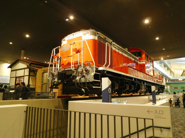 Roter und weißer Zug in einem Museum ausgestellt, Besucher, Informationsschild, Zaun und Deckenbeleuchtung.