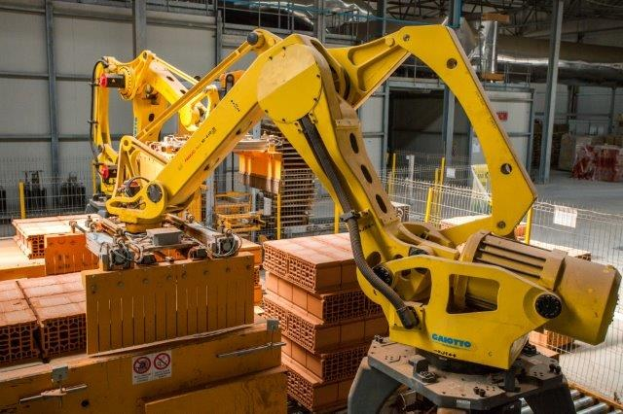 Großes Industriegebäude mit gestapelten Kisten, Überkopfkrane, Zaun, Strommasten und einer fernen Wand in einer automatisierten Fertigungsumgebung.