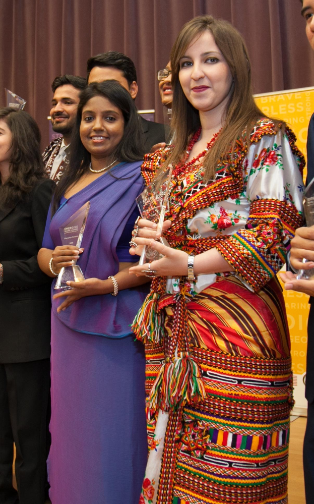 Gruppe von Menschen auf einer Bühne mit einer Frau, die eine Trophäe hält, vor einem Vorhang und einer Tafel mit der Aufschrift "Bravo Segen Award Gewinner."