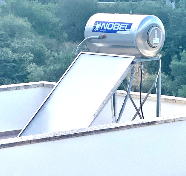 Solar-Wassererhitzer mit Speicher auf einem Gebäude montiert, Bäume im Hintergrund.