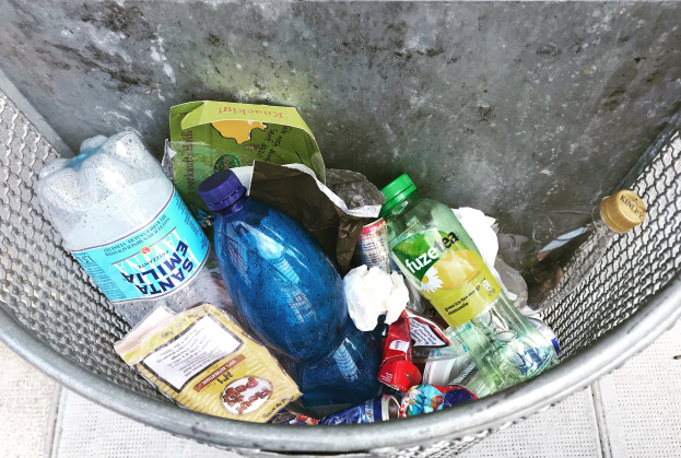 Ein Metallmüllcontainer voller verschiedener Plastikflaschen, Tüten und anderer Abfälle.