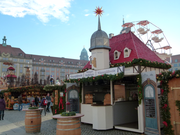 Ein geschäftiger Weihnachtsmarkt in Nürnberg, Deutschland mit Menschen um geschmückte Stände, festlicher Beleuchtung, einem Riesenrad im Hintergrund und einer Tafel mit Text auf der rechten Seite.