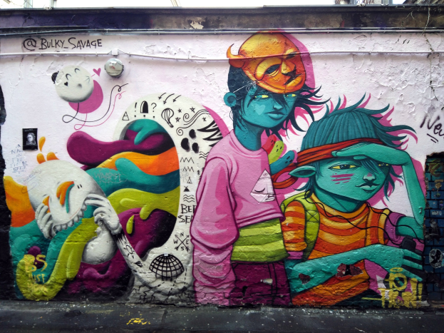 Mural an einem Gebäude mit Graffiti, das eine Straße am Boden, Pfähle im Hintergrund und einen klaren blauen Himmel zeigt.