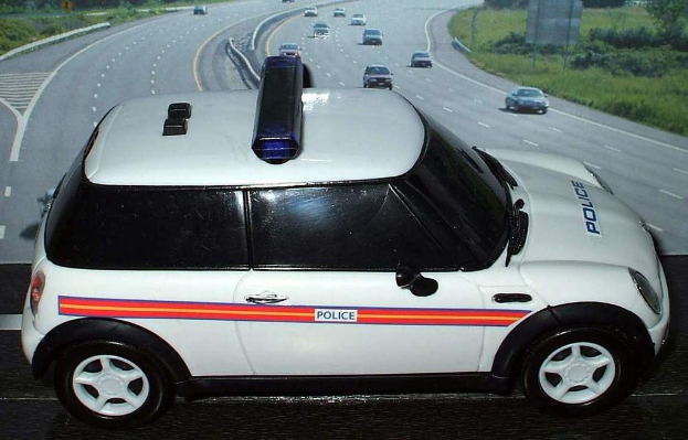 Weißer Polizeiwagen mit "Polizei"-Aufschrift auf einer Straße außerhalb der Stadt, umgeben von fahrendem Verkehr, Gras und Bäumen auf beiden Seiten.