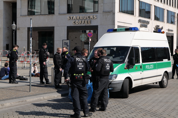 Polizisten vor einem Starbucks-Café mit einem Van auf der rechten Seite und Menschen auf der linken Seite, mit einem Gebäude, einem Schild, einem Laternenpfahl und einem Zaun im Hintergrund.