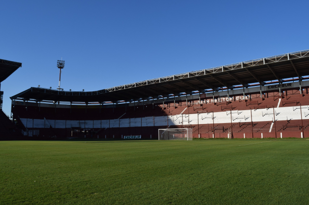 Ein Fußballfeld mit grünem Rasen, einem zentralen Torpfosten und einem beleuchteten Stadion im Hintergrund unter einem sichtbaren Himmel.