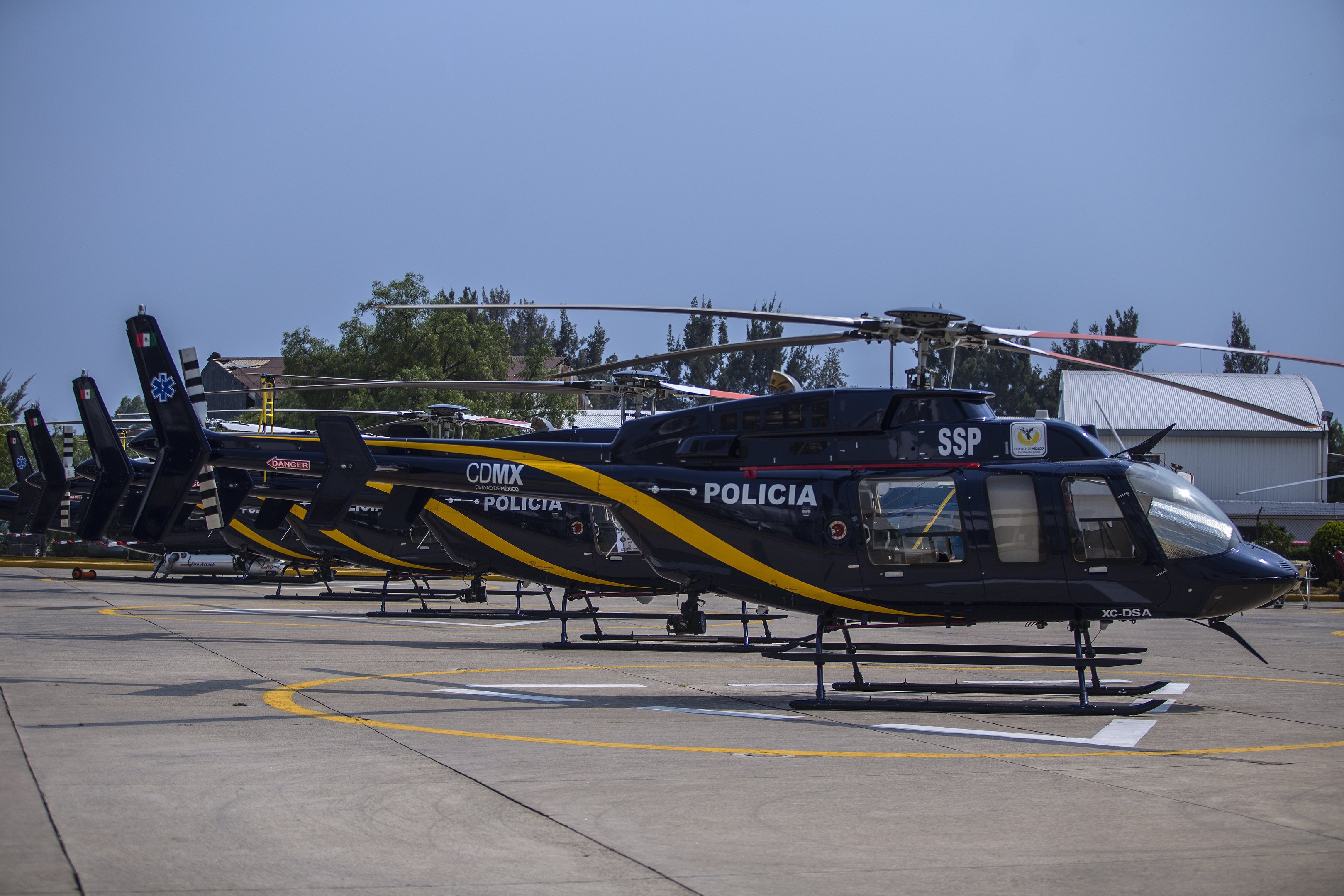 Polizeihubschrauber auf einem Flughafenvorfeld mit umliegenden Gebäuden, Bäumen und einem klaren blauen Himmel geparkt.